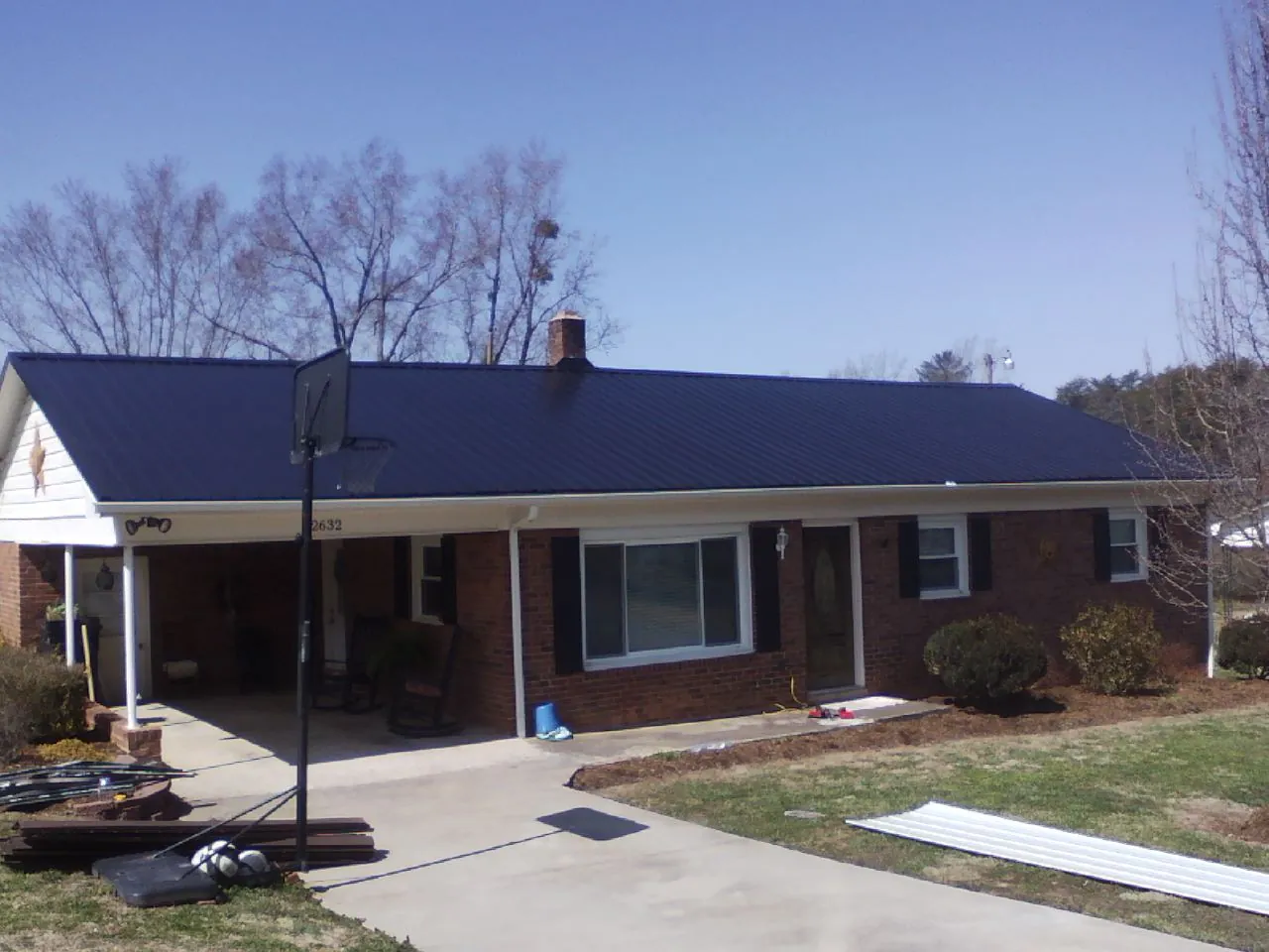 Finished dark blue metal roof on a brick ranch with a carport in Osage
