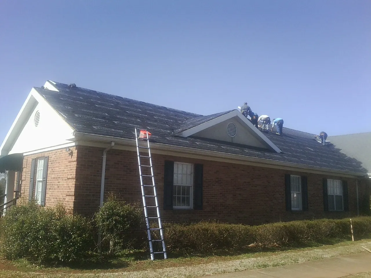 Crew tearing shingles off a brick ranch roof with a ladder set — Metal Roof Repair work by our crew in Osage