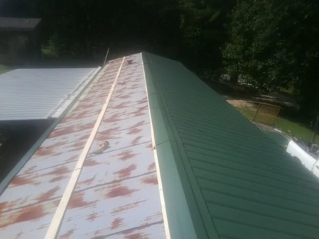 Old rusted panels beside newly installed green metal roofing — Wind Damage Roof Repair by Roofing Brothers in Osage